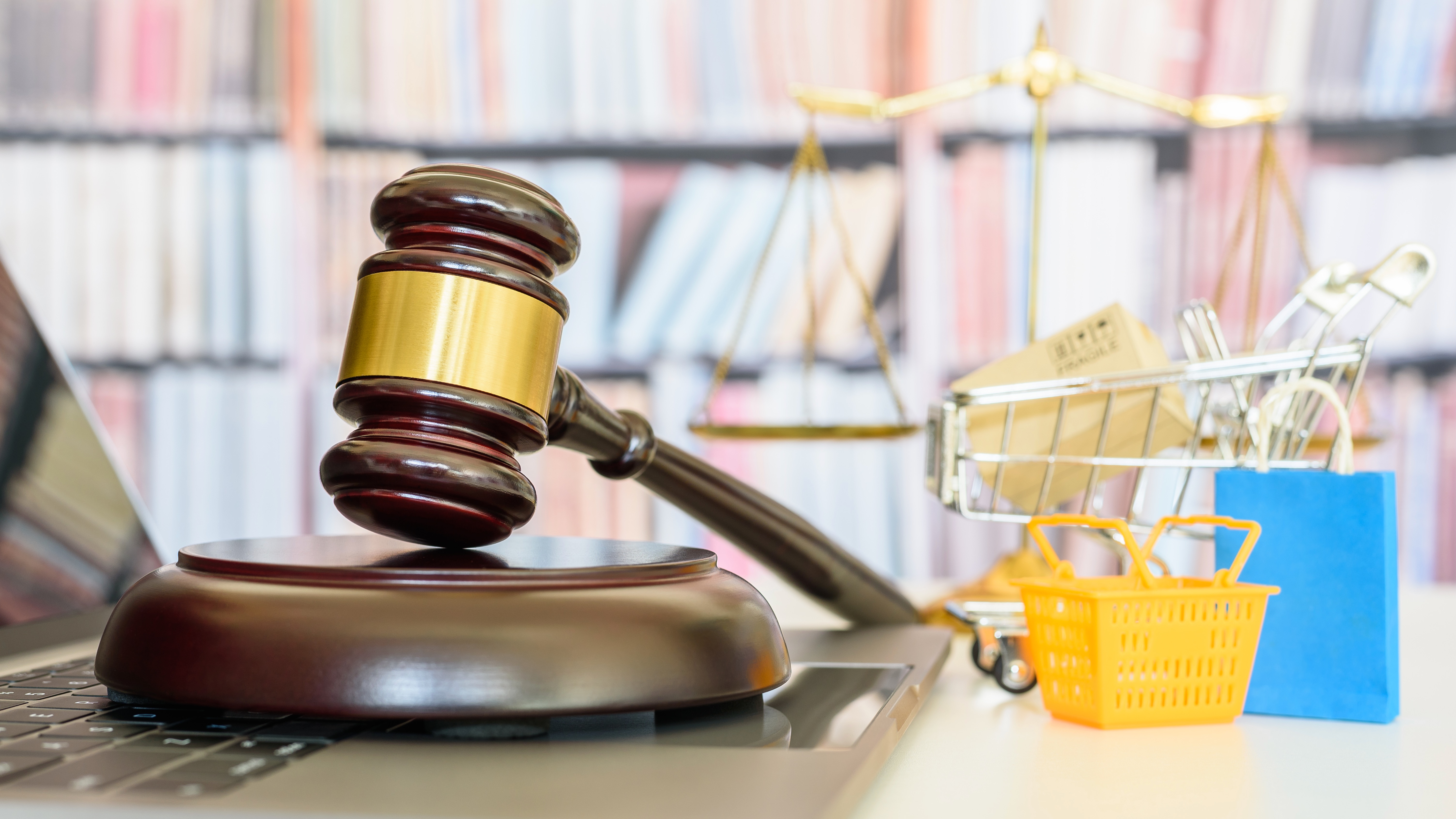 A judge's gavel on a laptop keyboard, with miniature shopping cart and basket beside it