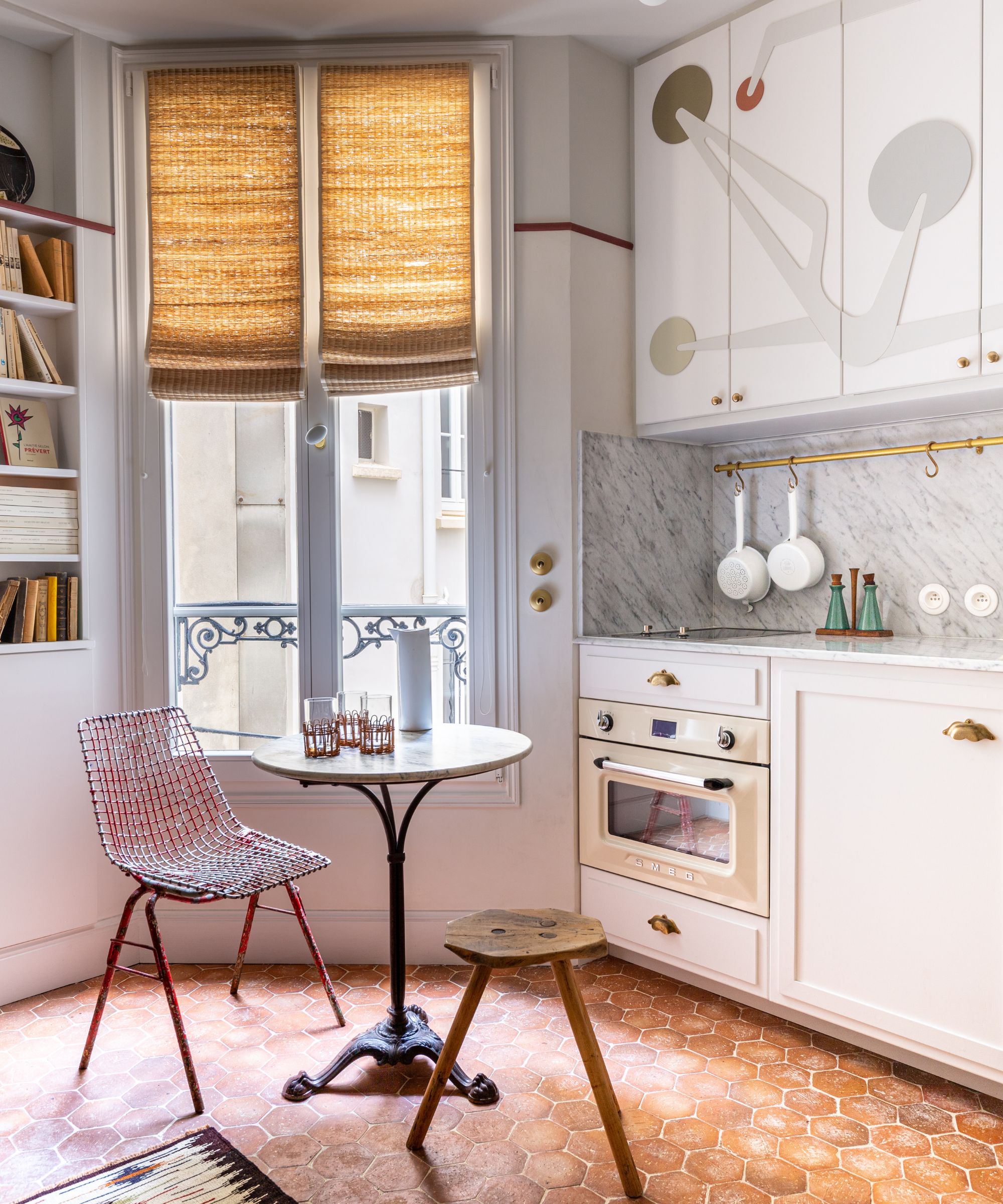 Parisian apartment with terracotta tiled floor, small table with chair and wooden stool and kitchen