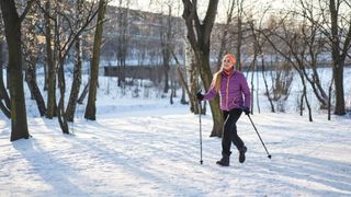 Woman Nordic walking through the snow with walking poles, wearing thick coat and head band
