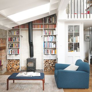 Log burner surrounded by shelves and books in a white living room with a blue sofa and footstool