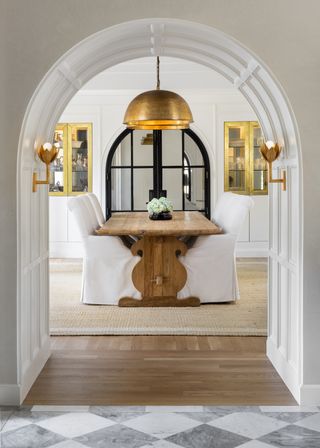 dining room with brass wall and ceiling lights, wood table and white chairs