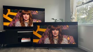 The LG G4 OLED TV on a TV bench, with LG G3 OLED next to it on the floor, and both showing the same scene of Bryce Dallas Howard in the movie Argylle