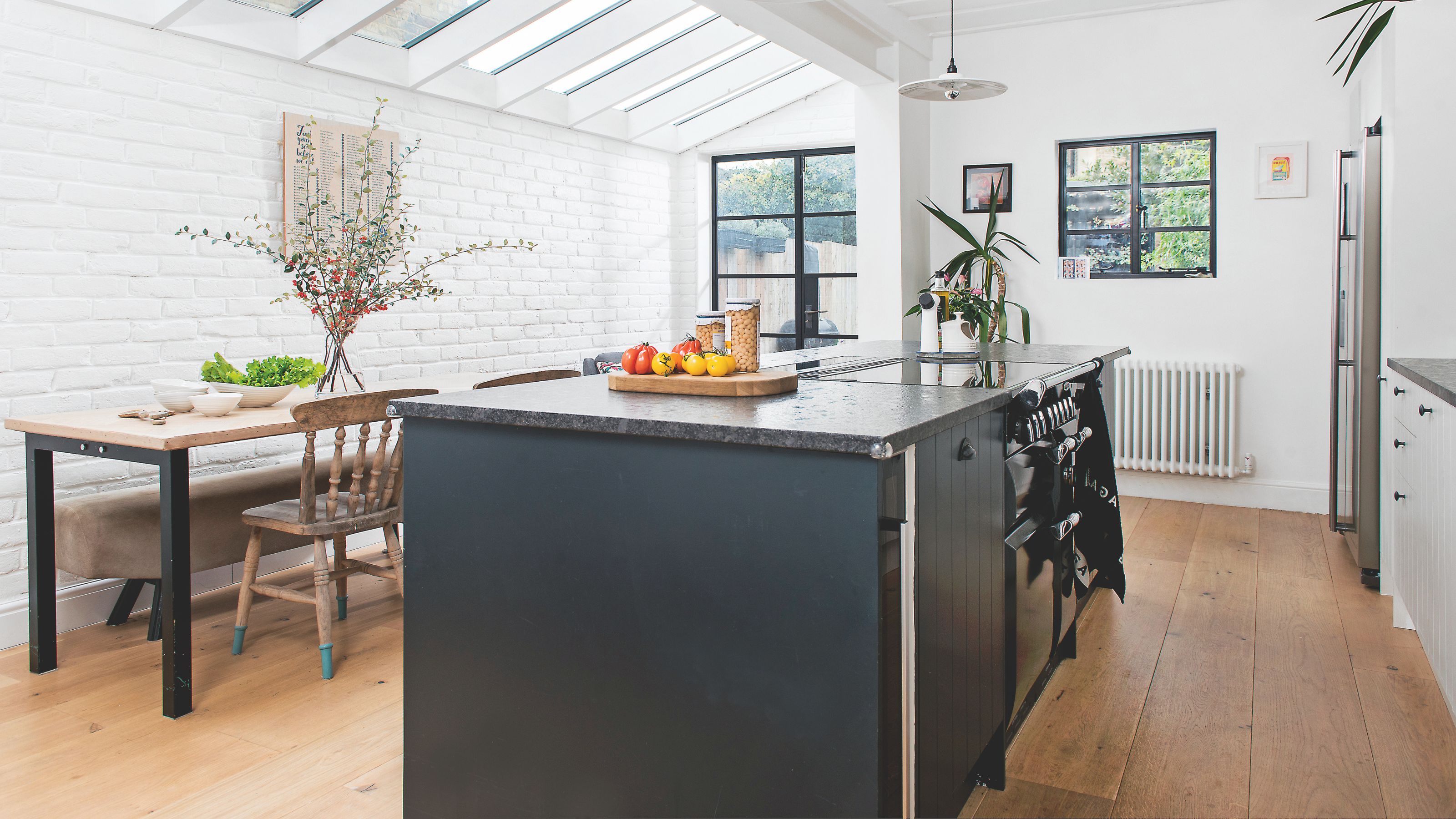 White kitchen-diner with a blue kitchen island and a wooden dining room table, with wooden flooring
