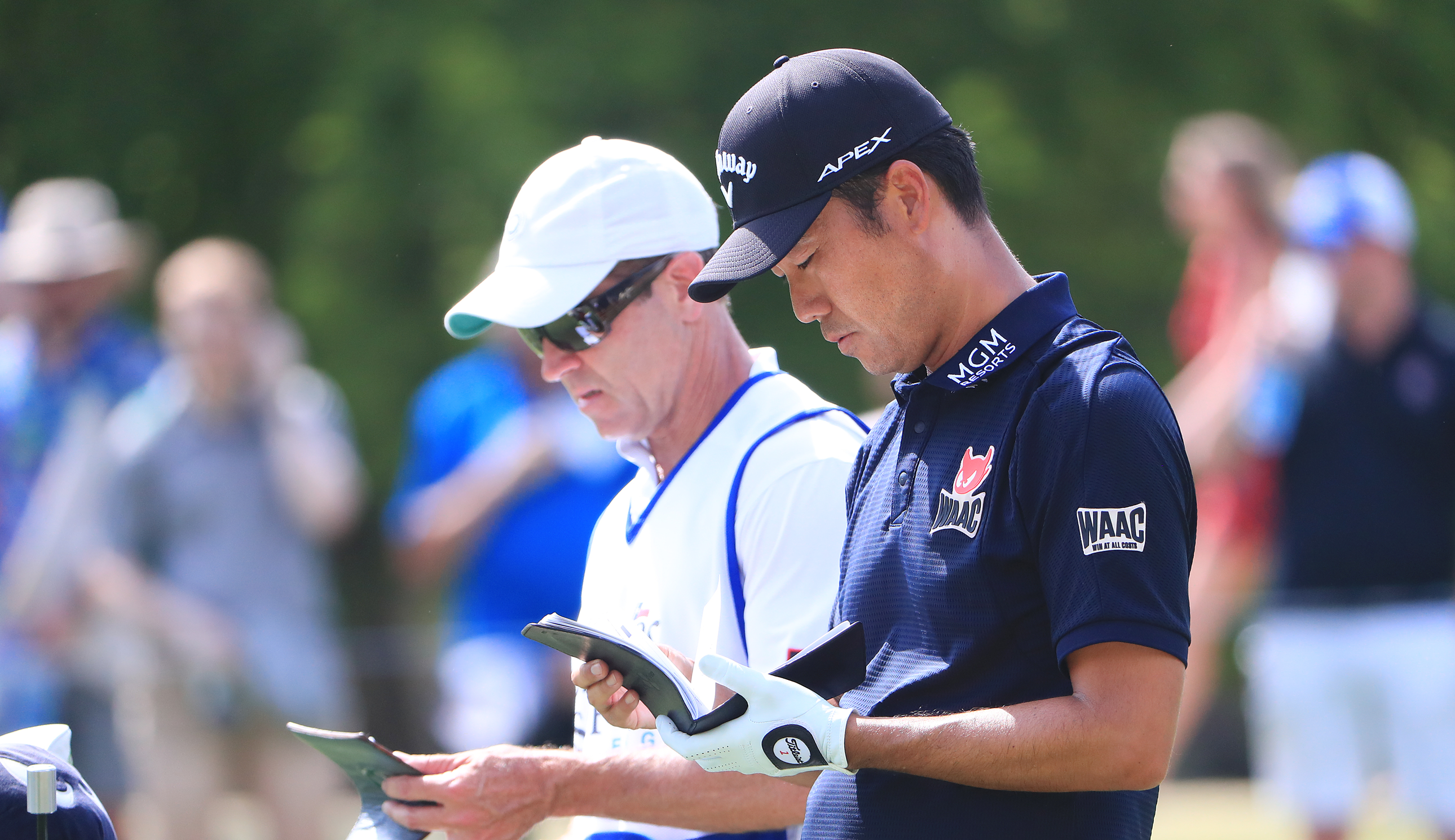 Kevin Na and Kenny Harms speak to each other while looking at a yardage book