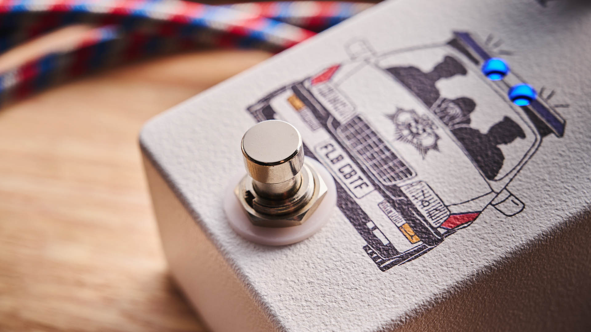 Funny Little Boxes Caught By The Fuzz: inspired by Supergrass, this two-knob fuzz has a white enclosure, blue dials, and a comic graphic of someone being apprehended in a police car.