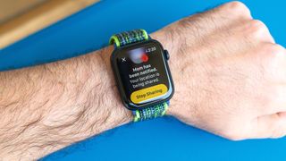 Detail shot of an Apple Watch SE on a bright blue background showing the steps to set up and send a Check In notification in watchOS 11