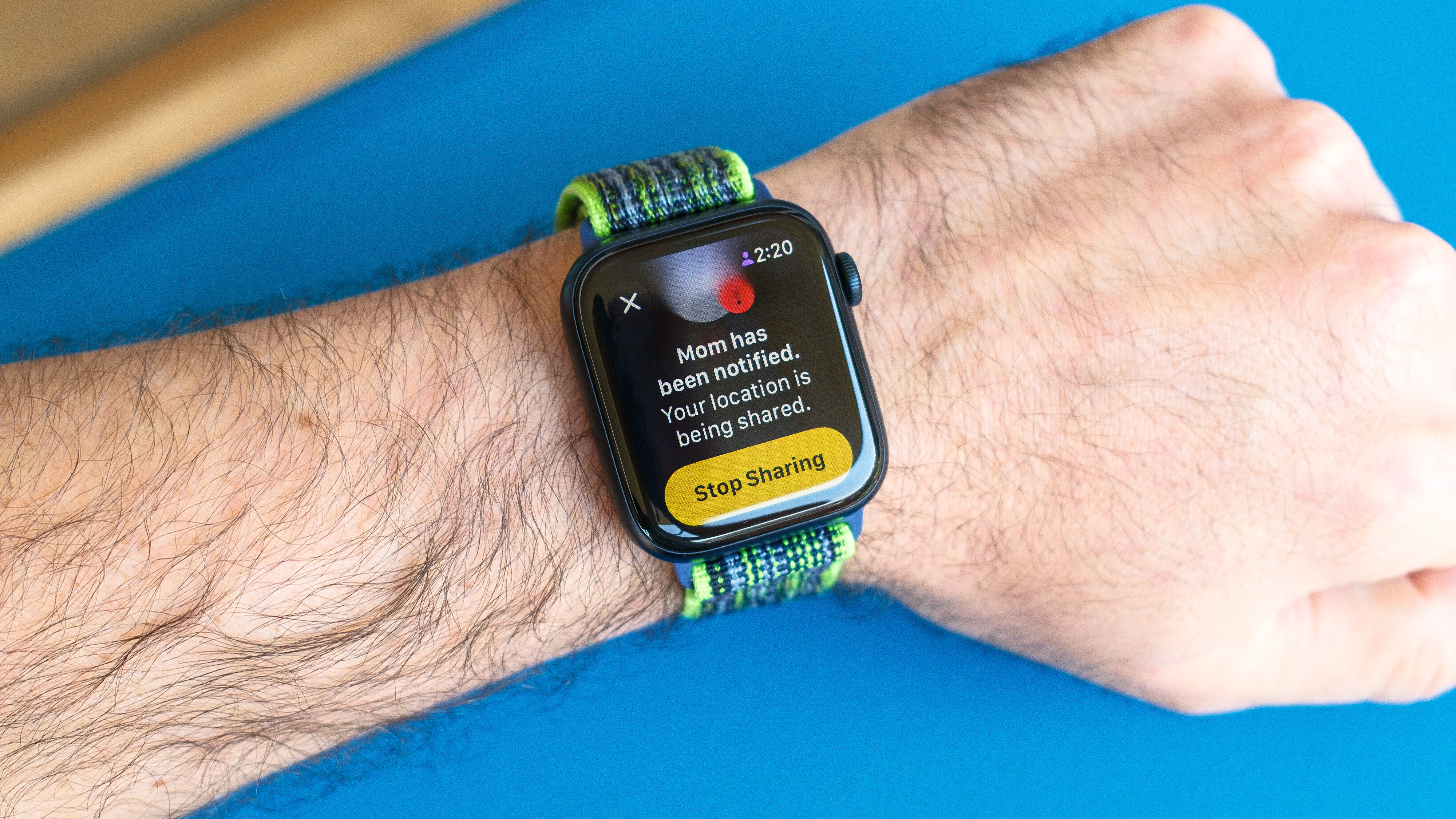 Foto detallada de un Apple Watch SE sobre un fondo azul brillante que muestra los pasos para configurar y enviar una notificación de Check In en watchOS 11