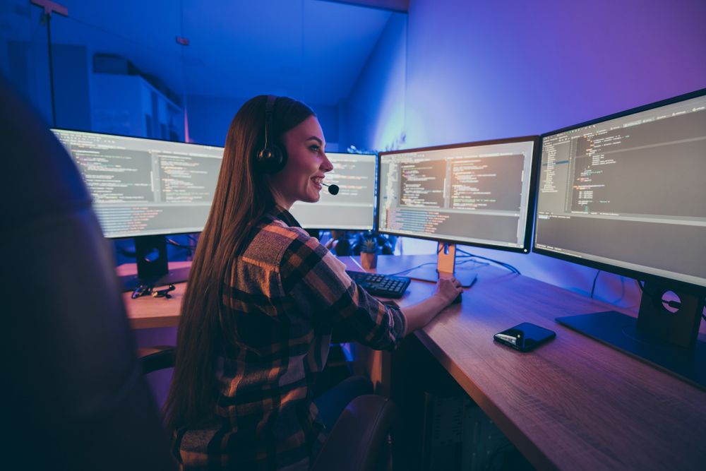 A female IT worker in front of multiple monitors displaying code