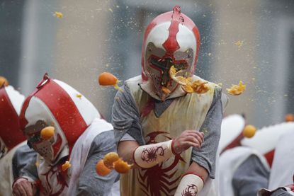 Costumed revelers in protective helmets throw oranges during Carnival in the northern Italian Piedmont town of Ivrea, Italy.