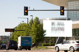 A busy road with vehincles with focus on a big white bill board with the text WE SHALL OVERCOME