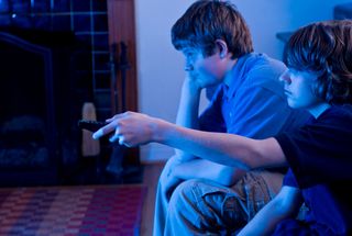 Two boys sit in a dark room watching television