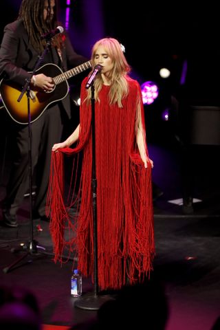 A photo of Suki Waterhouse swaying in a red fringe gown pulled from Calcaterra's Spring/Summer 2025 runway.