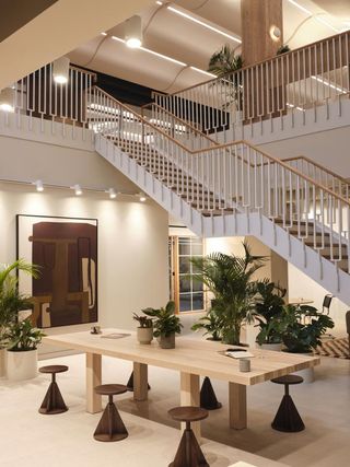 Large wood table with stools and various indoor pot plants. Stairwell rises above the area.