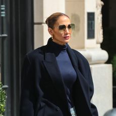 Jennifer Lopez wearing black coat, black turtleneck, blue jeans, blue boots, and sunglasses