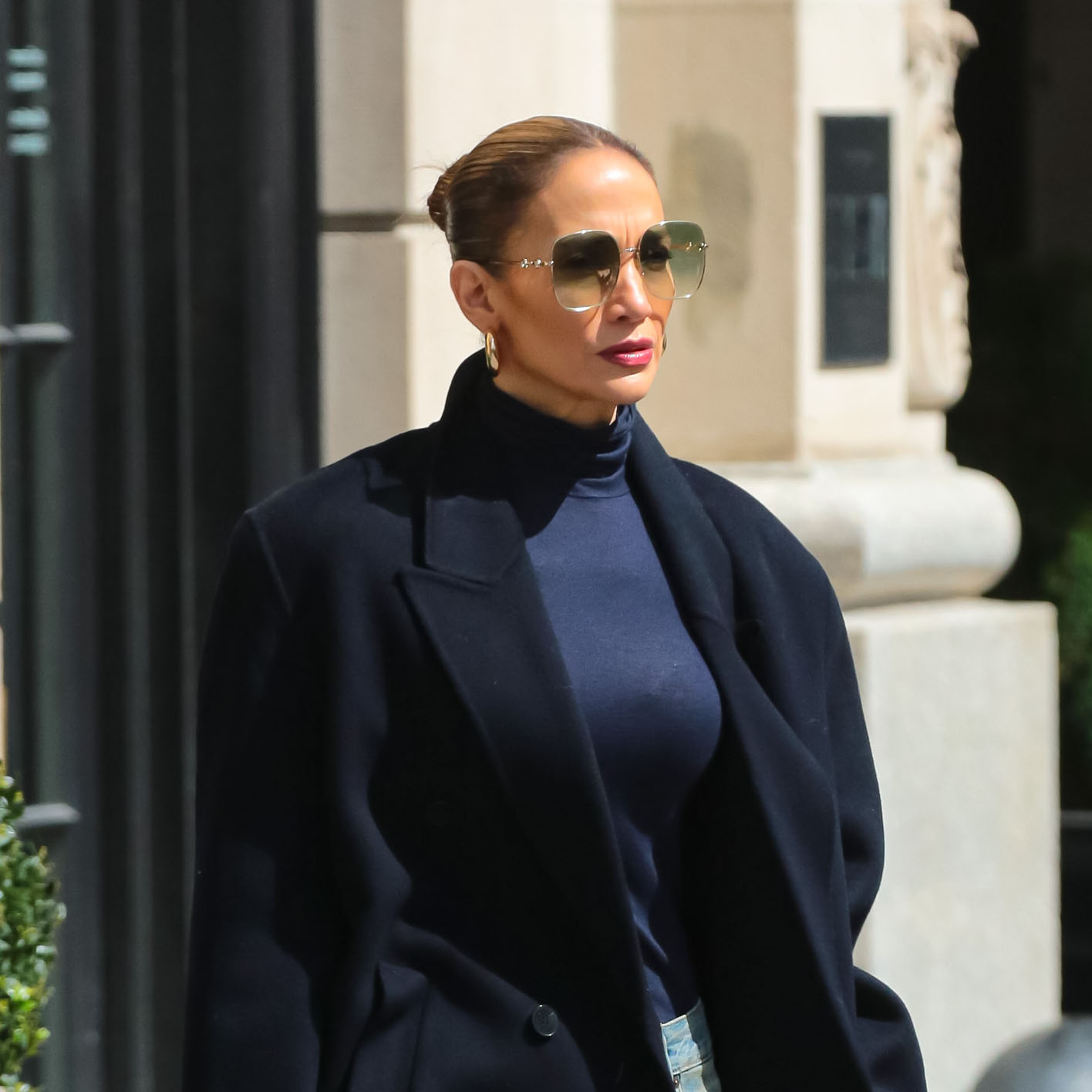 Jennifer Lopez wearing black coat, black turtleneck, blue jeans, blue boots, and sunglasses