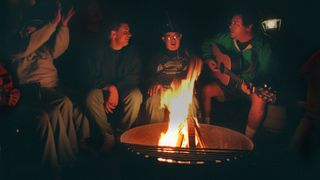 Man plays guitar around a campfire