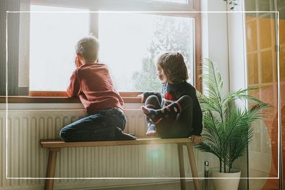 two children looking out of a sunny window from inside with their backs to the camera