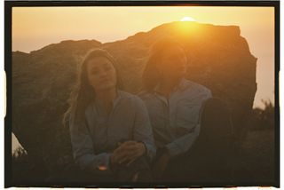 aj michalka and aly michalka sitting in front of a rock as the sun sets behind them