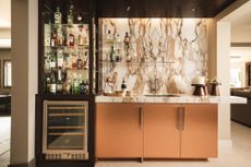 Home bar with copper cabinets and beige marbled backsplash