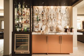 Home bar with copper cabinets and beige marbled backsplash