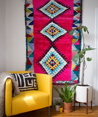 Colorful, patterned rug as wall art, with yellow armchair, and potted housesplants.