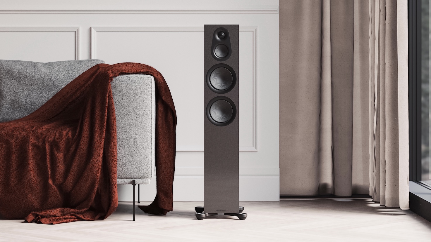 A Monitor Audio Silver Series 7G Limited Edition floorstanding speaker in its Carbon Black metallic finish between a grey sofa and a beige curtain in a living space.