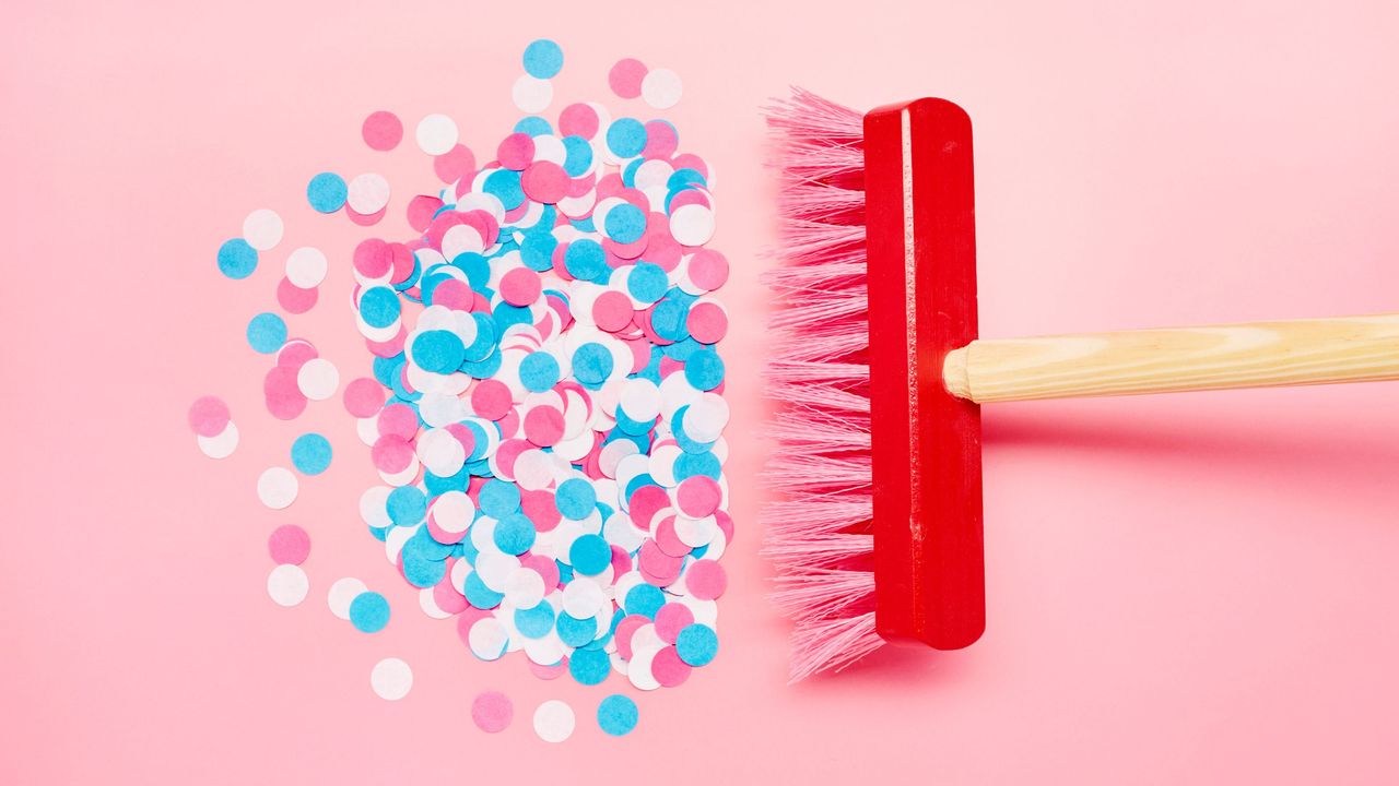 A red brush sweeping up colorful confetti on a pink background