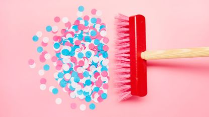 A red brush sweeping up colorful confetti on a pink background