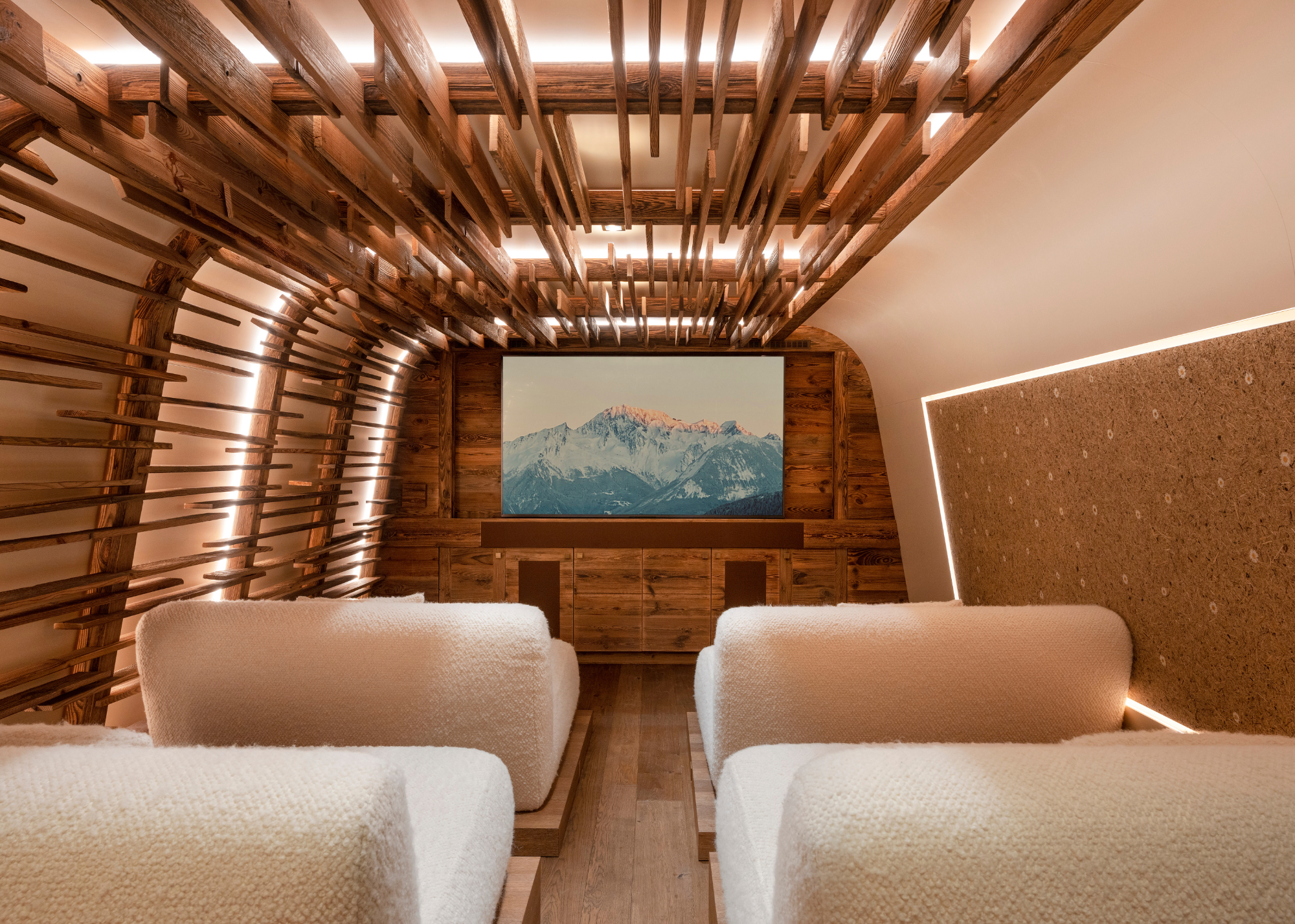 The cinema room at Refuge de la Traye with four very deep two-seater cream boucle sofas and wood planks decorated in an abstract pattern down one side of the wall and up and over the ceiling