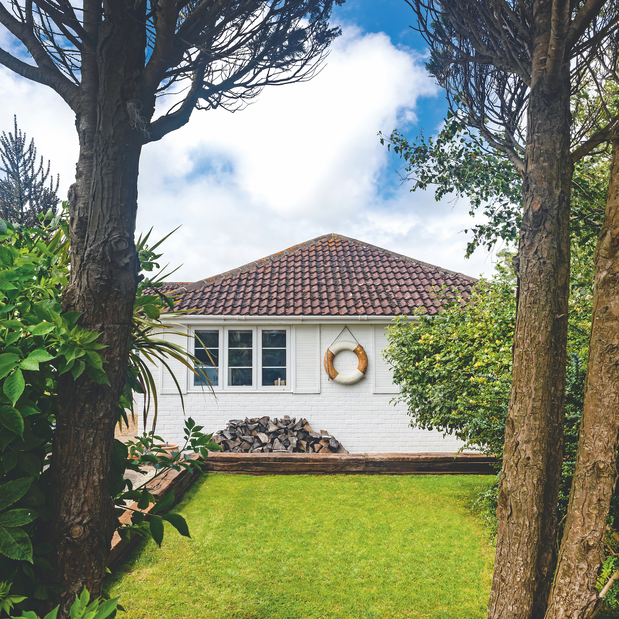 exterior of 1980s bungalow in Kent, UK, with white painted walls and life ring on wall, with grass lawn in front