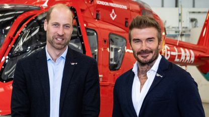 Prince William and David Beckham smiling in front of a helicopter