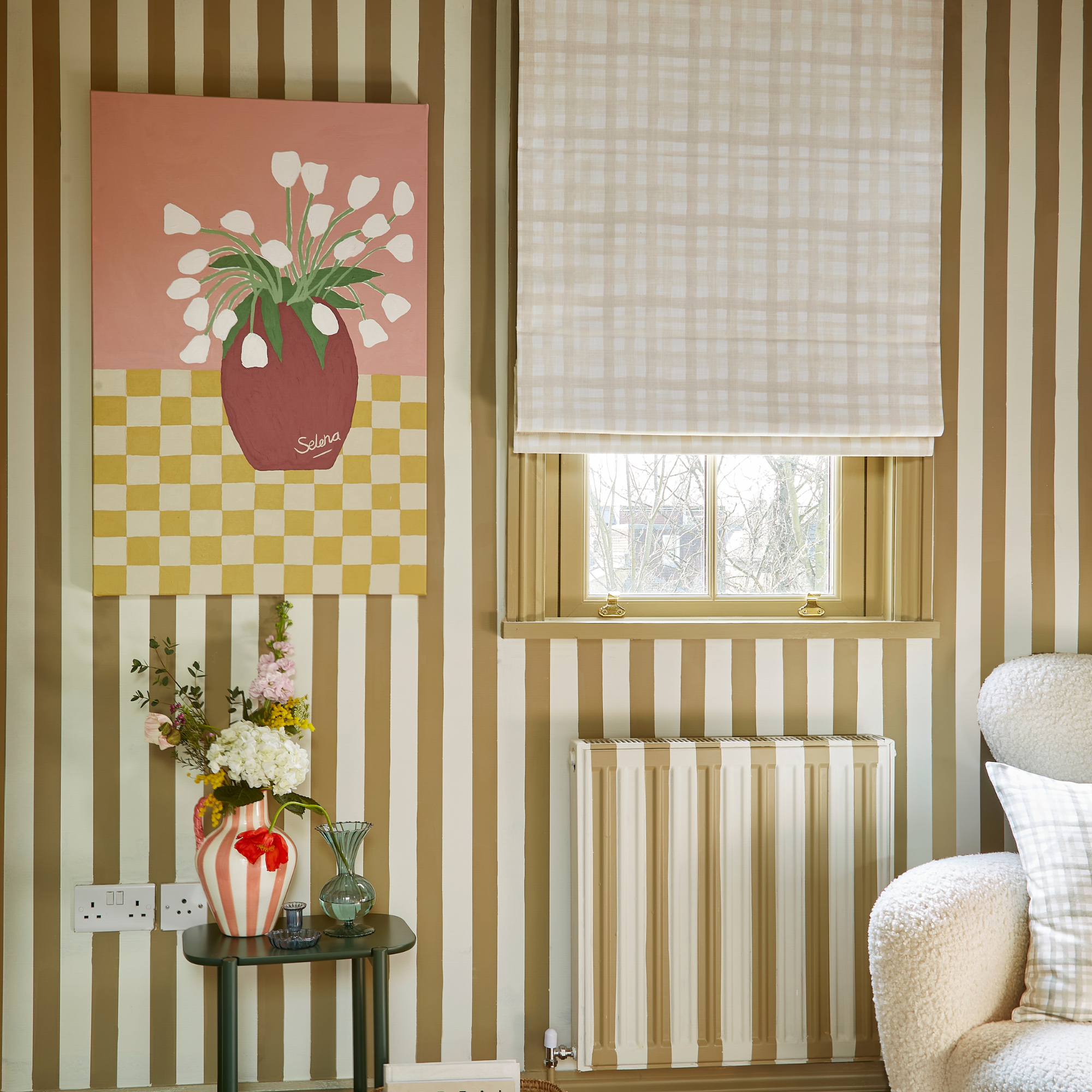 Brown and white striped wall and radiator, with beige roman vlinds and pink striped vase on green side table.