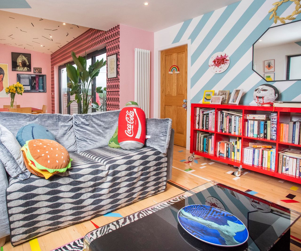 A living room with striped blue and white walls and sofa with burger and coca cushions