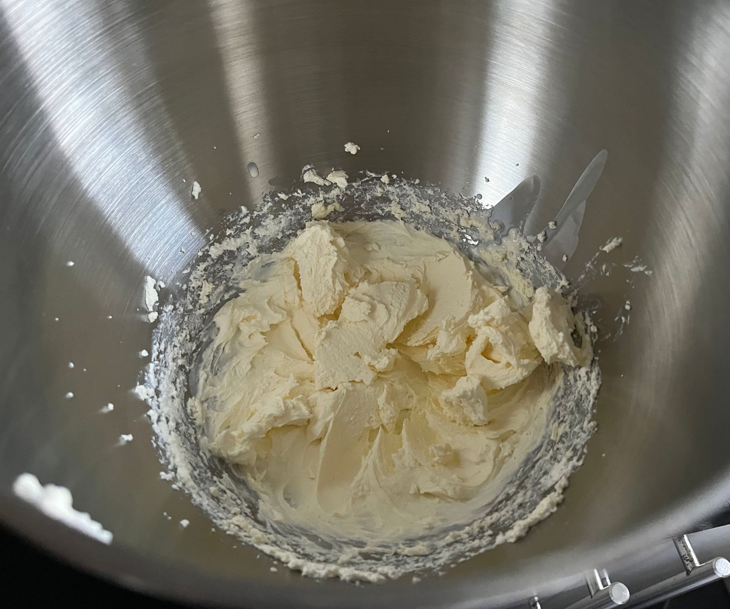 Thick whipped cream inside a stainless steel mixing bowl.
