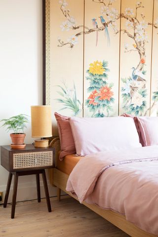 Bedroom with pink bedding, dark wood and rattan bedside table, yellow table lamp and yellow floral oversized mural headboard