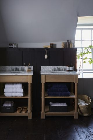 loft bathroom with dark wood paneling, black floorboards, two freestanding vanity units with open shelving, marble countertops