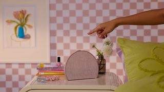 Rosy pink Hatch Restore 3 next to book, hair accessories and plant on bedside table in pink room with check wallpaper and green bedding