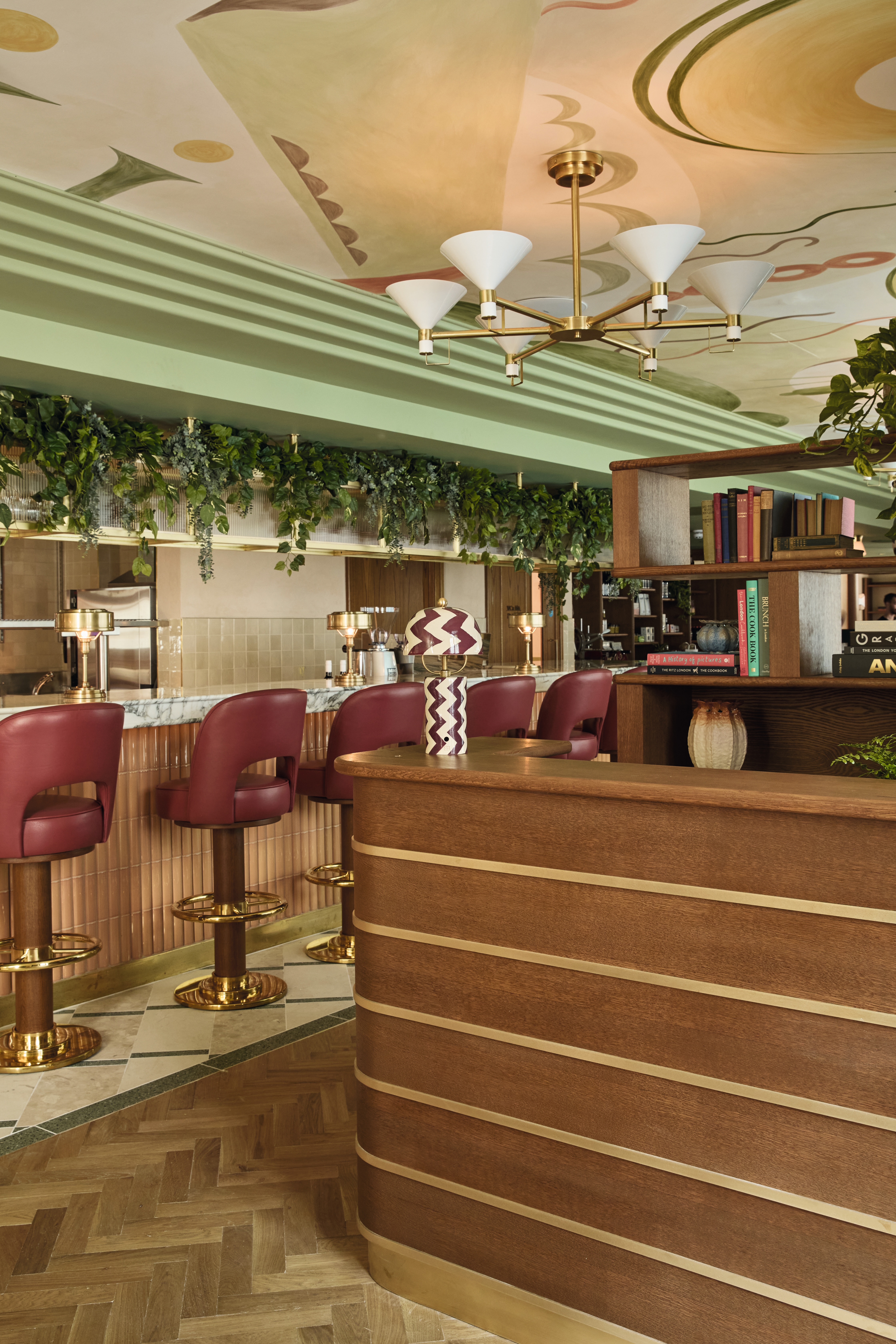 A dazzling bar with bordeaux leather stools, tiled and wooden surfaces, trailing plants, a ceiling mural, and a hip vibe.
