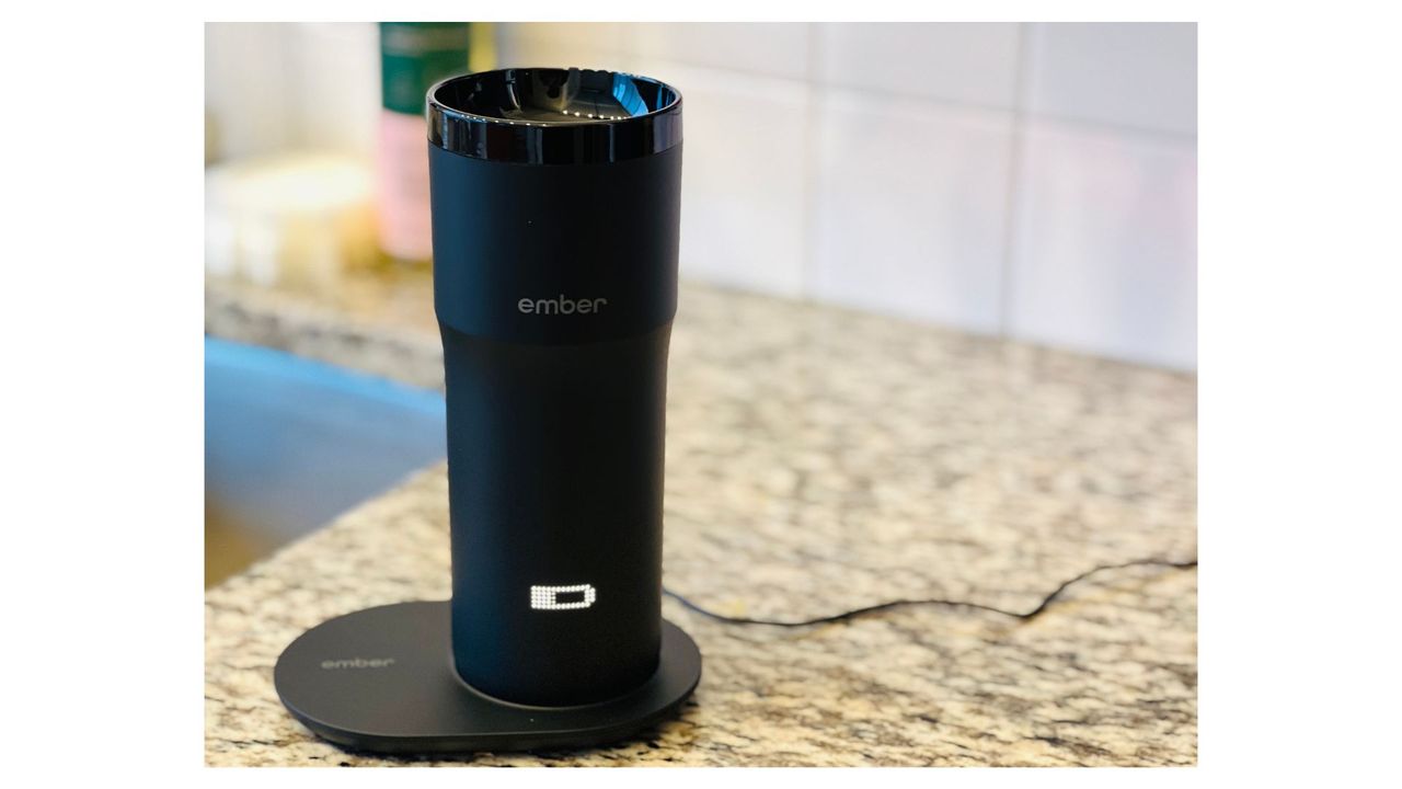A black Ember Travel Mug placed on a black charging coaster on a granite counter, for the best coffee travel mugs.