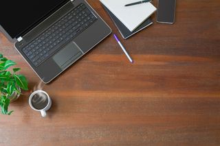 A laptop, notebook and cup of coffee on a dark wood desk