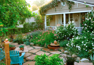 Front yard flower beds with white and pink blooms in an irregular paved yard.