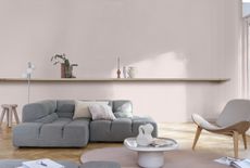 A modern living room with pale pink walls, a grey modular sofa, and open shelving 