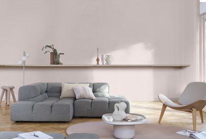 A modern living room with pale pink walls, a grey modular sofa, and open shelving 