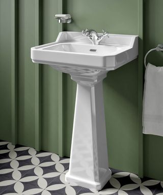 A traditional pedestal sink with a crisp white finish, set against a deep green panelled wall