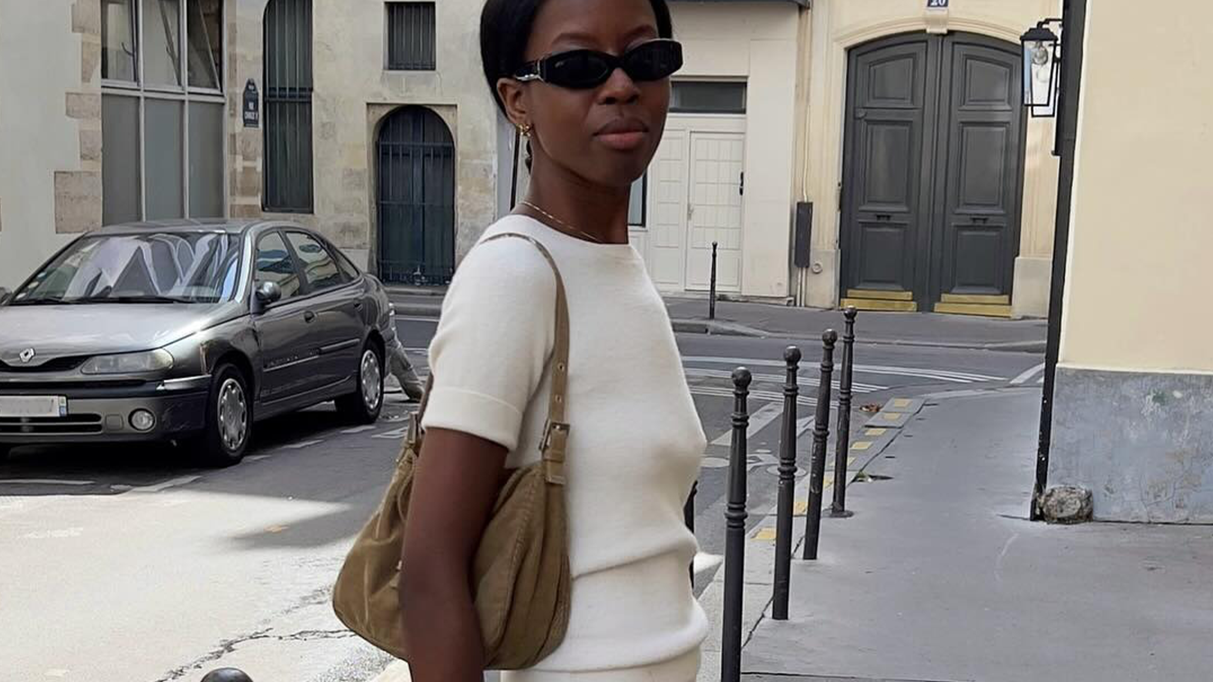 Woman wearing white cashmere t-shirt, white maxi skirt, brown bag, and black oval sunglasses on the streets of Paris.