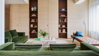 a Milanese flat designed to feel like a london apartment with large pale wood storage and green velvet couches in the living area