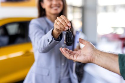Dealer handing car key to businessman with electric SUV in background inside car dealership, symbolizing sustainable transportation, vehicle purchase, and business success.