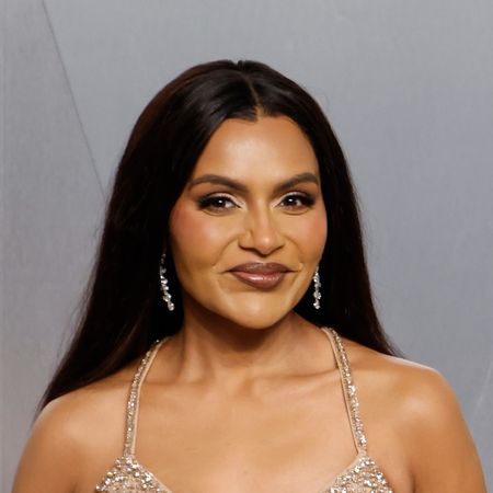 a woman with dark hair poses in front of a gray background at a red carpet event