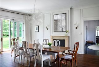 formal dining room with stone fireplace and long polished wood table painted white dining chairs and wooden chairs at head of table with French door open to garden