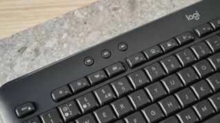 a black full sized keyboard with batteries and a palm rest on a clean beige surface with a blue backdrop